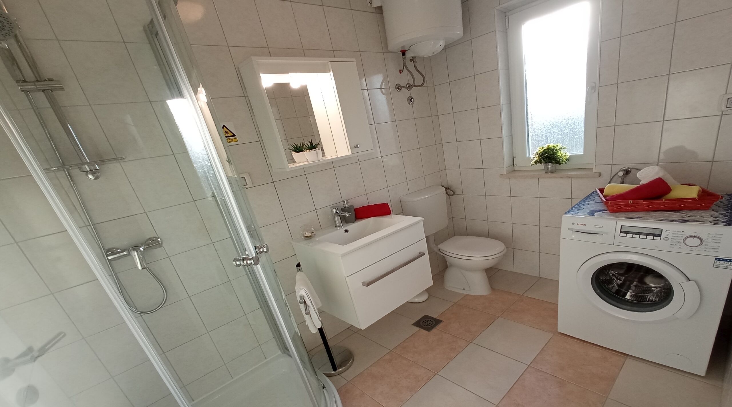 A bathroom with a glass shower enclosure, a white sink, a toilet, and a washing machine.