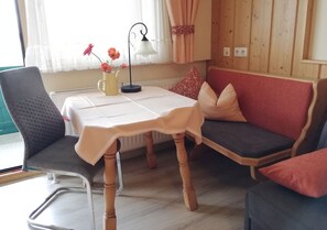 A cozy room with a wooden table, a grey chair, a red sofa, and a lamp.