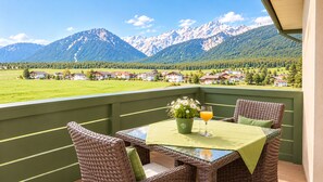 A balcony with wicker furniture, a table with a green tablecloth, a glass of orange juice, and a potted plant with white flowers.