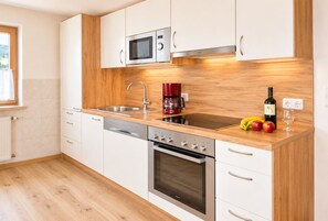 A modern kitchen with white cabinetry, a stainless steel microwave, a coffee maker, and a wine bottle on the counter.