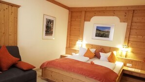 Une chambre à coucher aux murs lambrissés, comprenant un lit, deux tables de chevet, une commode, un canapé et deux tableaux encadrés accrochés au mur.