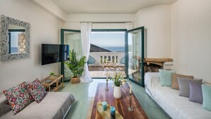 A modern living room with a sofa, a coffee table, and a TV. There is a balcony with a view of the sea. - Villa Phaedra 7 bedroom villa (Tersanas)