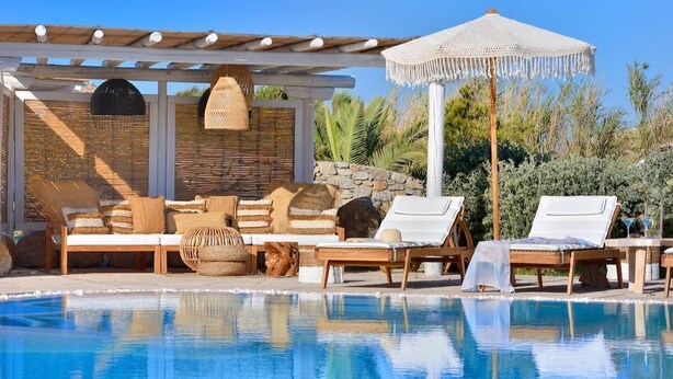 Et poolområde med liggestole, et pergola og en parasol af fletmateriale.