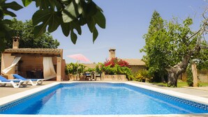 Una piscina con sillas de descanso, un área de estar techada y un edificio con tejado de azulejos.