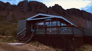 Een houten chalet met een balkon, een trap en uitzicht op een bergachtig landschap.