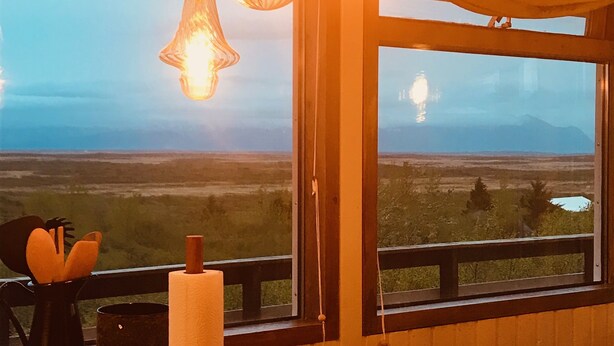 Een keuken met een houten aanrechtblad, hangende hanglampen en een uitzicht op een landschap in de verte door een groot raam.