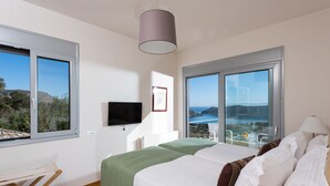 A modern bedroom with a bed, a TV, and large windows offering a scenic view. - Amazing Sea View to Spinalonga Island - 3 bedroom villa (Elounda)
