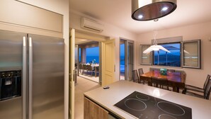 A modern kitchen with a built-in stove, a large refrigerator, and a dining area with a table and chairs. - Amazing Sea View to Spinalonga Island - 3 bedroom villa (Elounda)