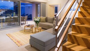 A modern living room with a staircase, a sofa, a coffee table, and a dining area with chairs and a table. - Amazing Sea View to Spinalonga Island - 3 bedroom villa (Elounda)