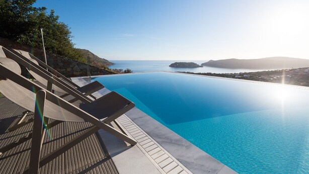 A clear blue infinity pool with lounge chairs and a stone deck, overlooking a calm sea and distant islands. - Amazing Sea View to Spinalonga Island - 3 bedroom villa (Elounda)