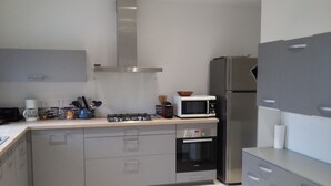 Une cuisine moderne avec des meubles gris, une hotte en acier inoxydable, un four à micro-ondes, une cuisinière à gaz et un four encastré.