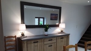 Un coin repas comprenant un buffet en bois, deux chaises, une table recouverte d’une nappe à motifs floraux, une plante en pot et un miroir fixé au mur.