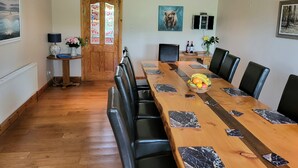 A dining area with a long wooden table, black leather chairs, and a fruit bowl. - Spectacular Views, Miles of Beaches, and Boat Trips, 4 Star  Luxury Home (Dingle)