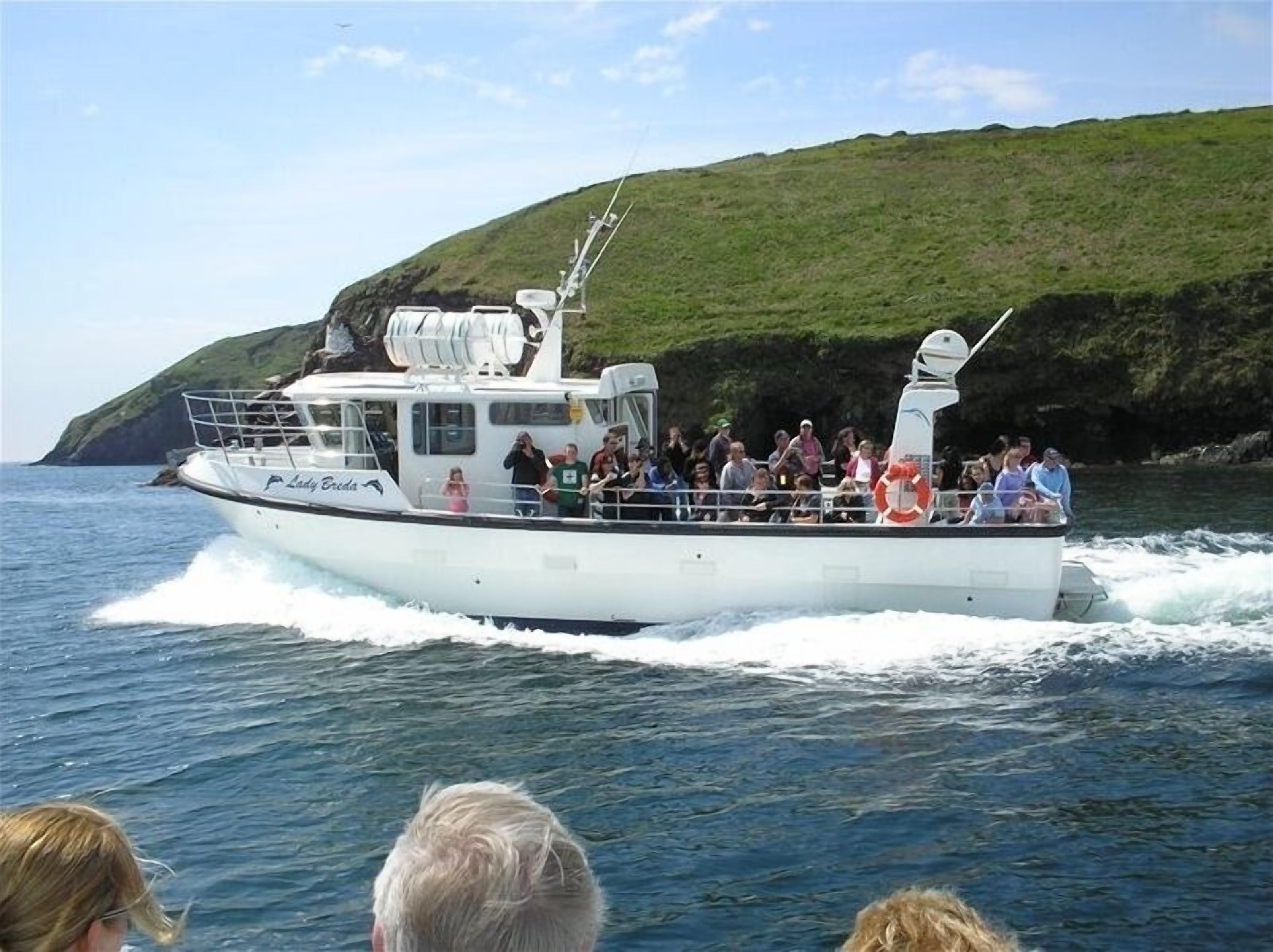 Ein Boot mit Passagieren fährt durch ein Gewässer, im Hintergrund eine hügelige Landschaft.
