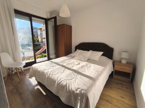 Ein Schlafzimmer mit Bett, Sessel, Nachttisch und Blick auf einen Balkon.