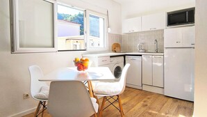 A compact kitchen with white appliances, a dining table with chairs, and a view of a residential area through the windows. - Bright 1BR apartment with two balconies, mountain views, sea glimpses and PKG (Будва)