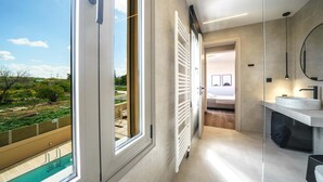 A modern bathroom with a large window, a white radiator, and a sink with a round mirror. - Luxury, Spacious Villa with private gym, just 4km from the sandy beach! (Πηγή)