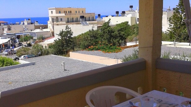 Varanda com mesa posta para refeições, com vista para área costeira, edifícios e o mar.
