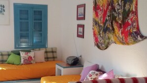 Quarto com cama, sofá, mesa, tapeçaria colorida e janela com persianas azuis.