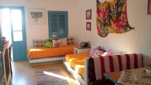 Quarto com duas camas, um sofá, uma mesa e uma janela com persianas azuis.