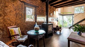 Un interior rústico con paredes de piedra, techo de madera, chimenea y vistas al exterior.