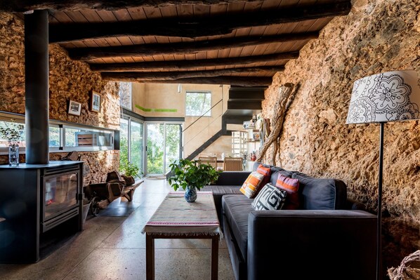 A cozy living room with a fireplace, a sofa with colorful cushions, and a view of a rustic stone wall. - Bau Ksar Casas Valdelarco for 4 people (Valdelarco)