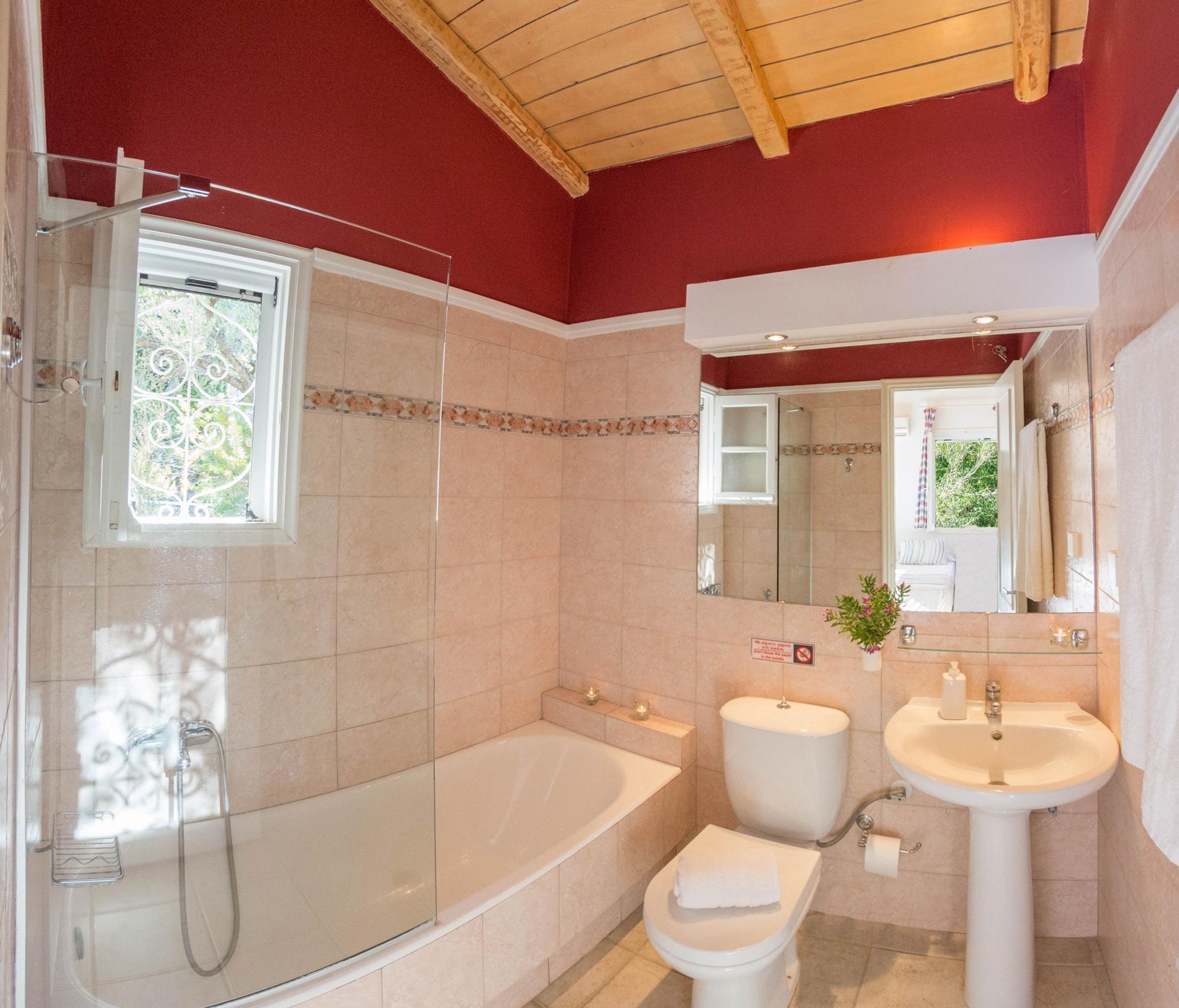 A bathroom with a bathtub, toilet, and sink, featuring a red wall and a wooden ceiling.