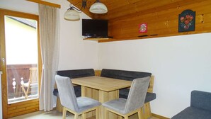 A room with a wooden ceiling, a TV mounted on the wall, a wooden dining table with chairs, and a sofa. - Haus Schneeberg - Aberg - Family apartment sleeping up to 5 people, with Hochkönig Card (Mühlbach am Hochkönig)