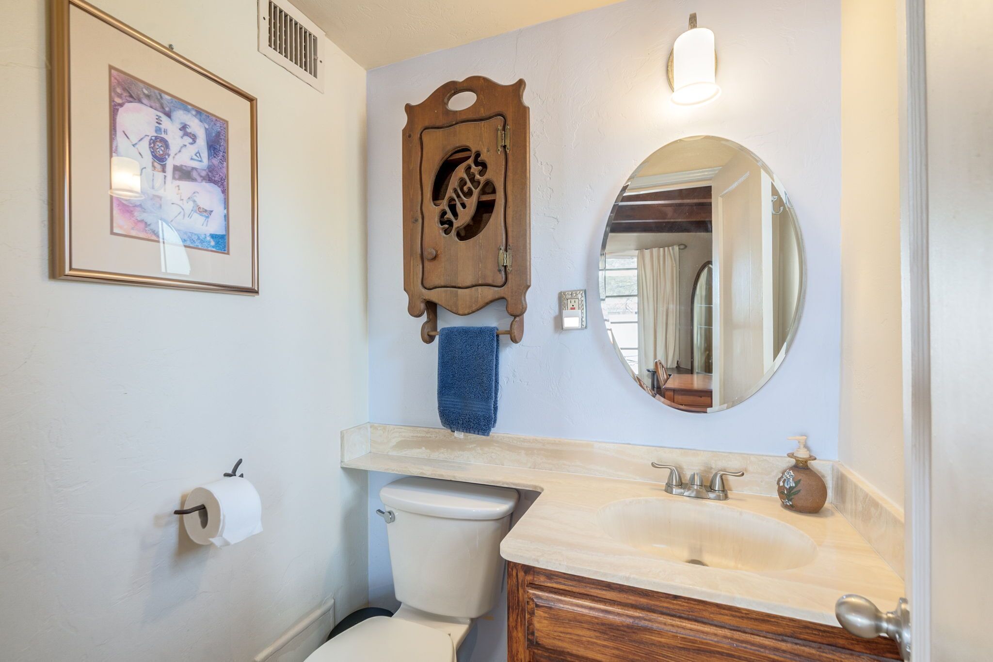 A bathroom with a toilet, sink, mirror, towel rack, framed artwork, and a decorative wooden panel.