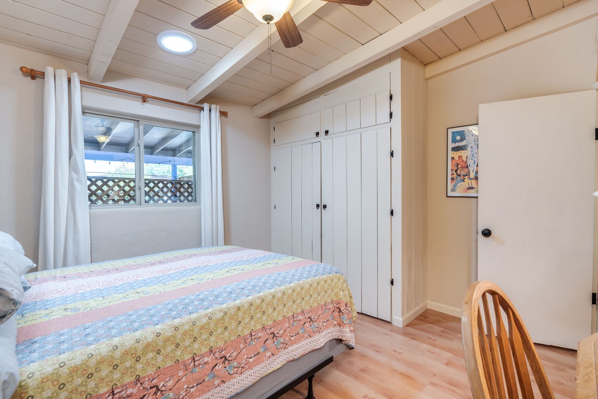 Un dormitorio con cama, ventilador de techo, ventana con cortinas, armario y puerta.