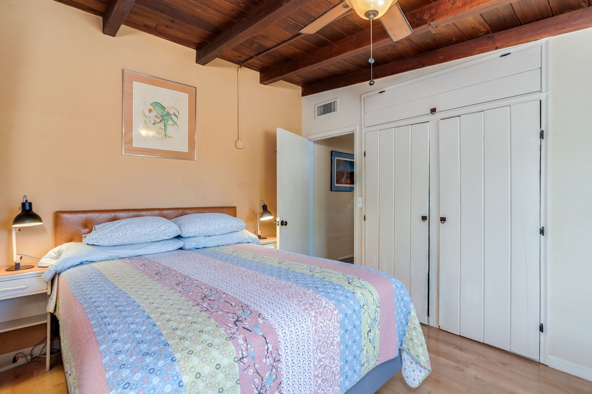 Ein Schlafzimmer mit Bett, Nachttisch, Lampe, Kleiderschrank und Deckenventilator.