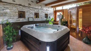 Un área de spa con jacuzzi, pared de piedra, vigas de madera y plantas en macetas.
