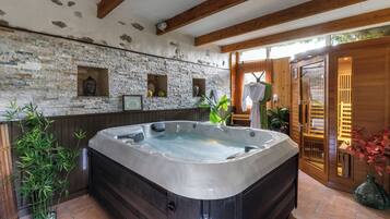 Ein Wellnessbereich mit Whirlpool, Steinwand, Holzbalken und Topfpflanzen.
