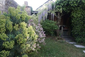 Een weelderige tuin met diverse planten en een stenen gebouw op de achtergrond.
