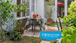 Un patio con mesa y sillas, una sombrilla roja y plantas en macetas.