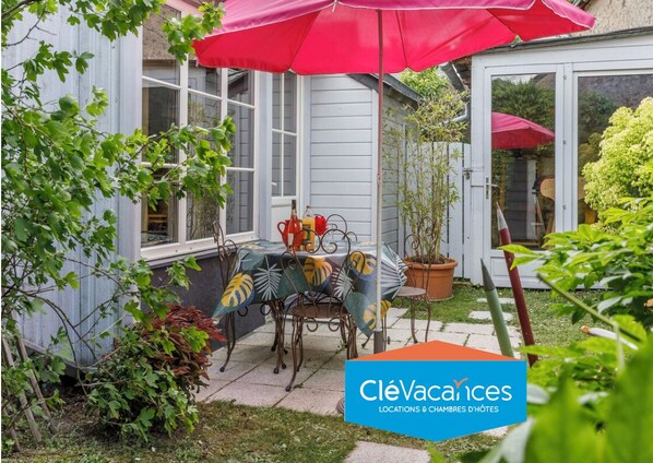 Une terrasse avec une table et des chaises, un parasol rouge et des plantes en pot.