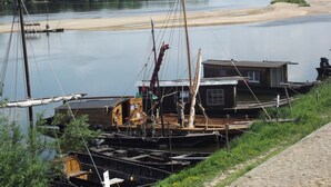 Un muelle a la orilla del río con una casa flotante de madera, un muelle pequeño y una playa arenosa.