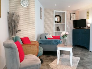A living room with a grey sofa, a wicker chair, a blue armchair, and a small white table with a vase.