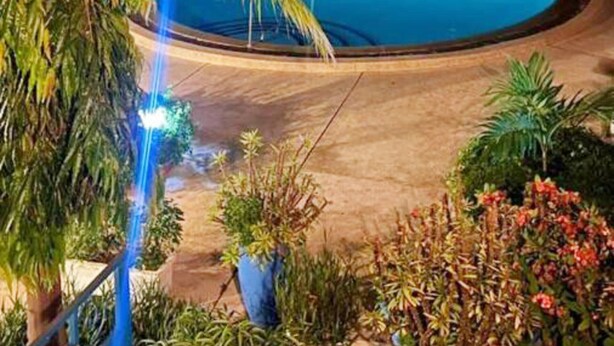 A nighttime view of a swimming pool surrounded by palm trees and a building.