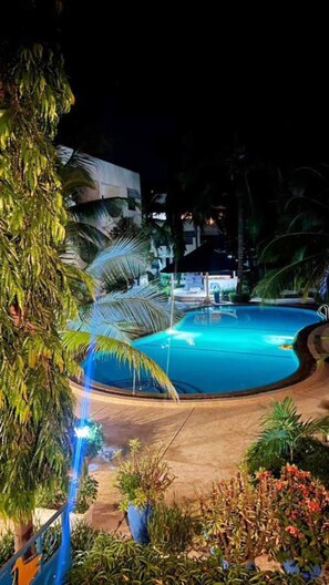 Une vue nocturne d’une piscine entourée de palmiers et d’un bâtiment.