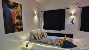A modern bedroom with a bed, bedside lamps, a wall art piece, and a decorative wall quote.