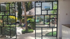 A room with a large glass door leading to an outdoor area with a thatched-roof structure and greenery.