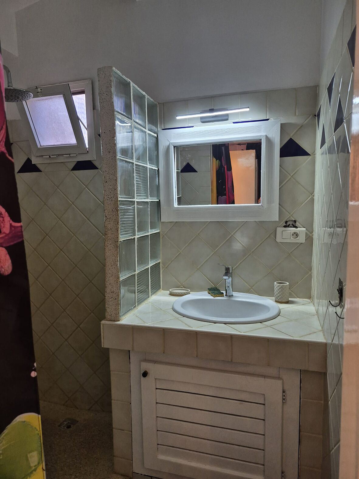 A bathroom with a sink, mirror, and shower enclosure.