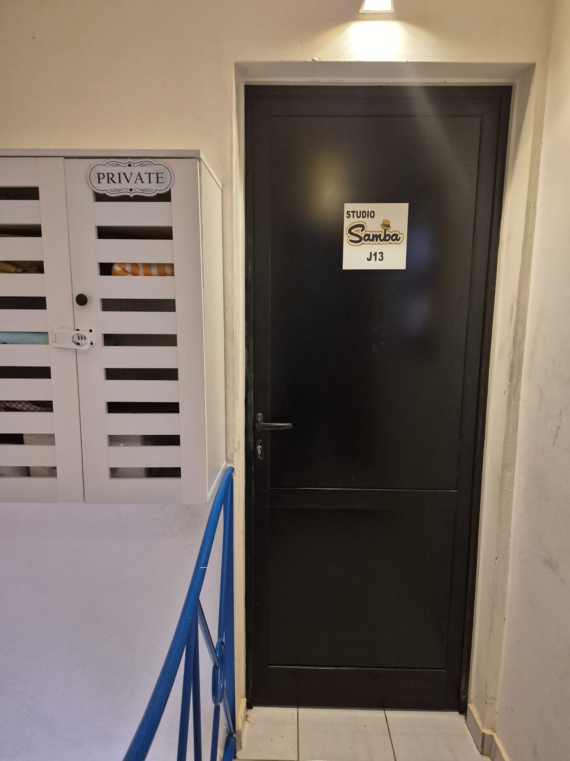 Une porte en bois donnant sur un studio privé, portant l’inscription « Studio Samba J13 », avec une poignée en métal et un trou de serrure.