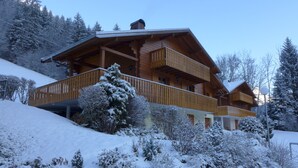 Un chalet en bois doté d’un balcon, entouré d’arbres couverts de neige et surmonté d’un toit à pente.