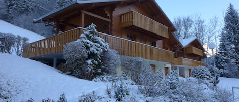 Una cabaña de madera con balcón, rodeada de árboles cubiertos de nieve y un techo inclinado.