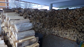 Une pile de bois de chauffage, placée sous un abri et protégée par une rambarde en métal.