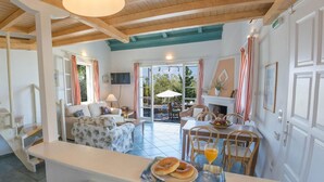 A spacious living area with a sofa, dining table, and chairs. A breakfast tray with bagels and juice is on the counter. - Villa Kiparissi - Agios Nikitas Villas (Άγιος Νικήτας)