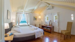 A bedroom with a bed, bedside table, lamp, chair, and a view of the sea. - Villa Kiparissi - Agios Nikitas Villas (Άγιος Νικήτας)