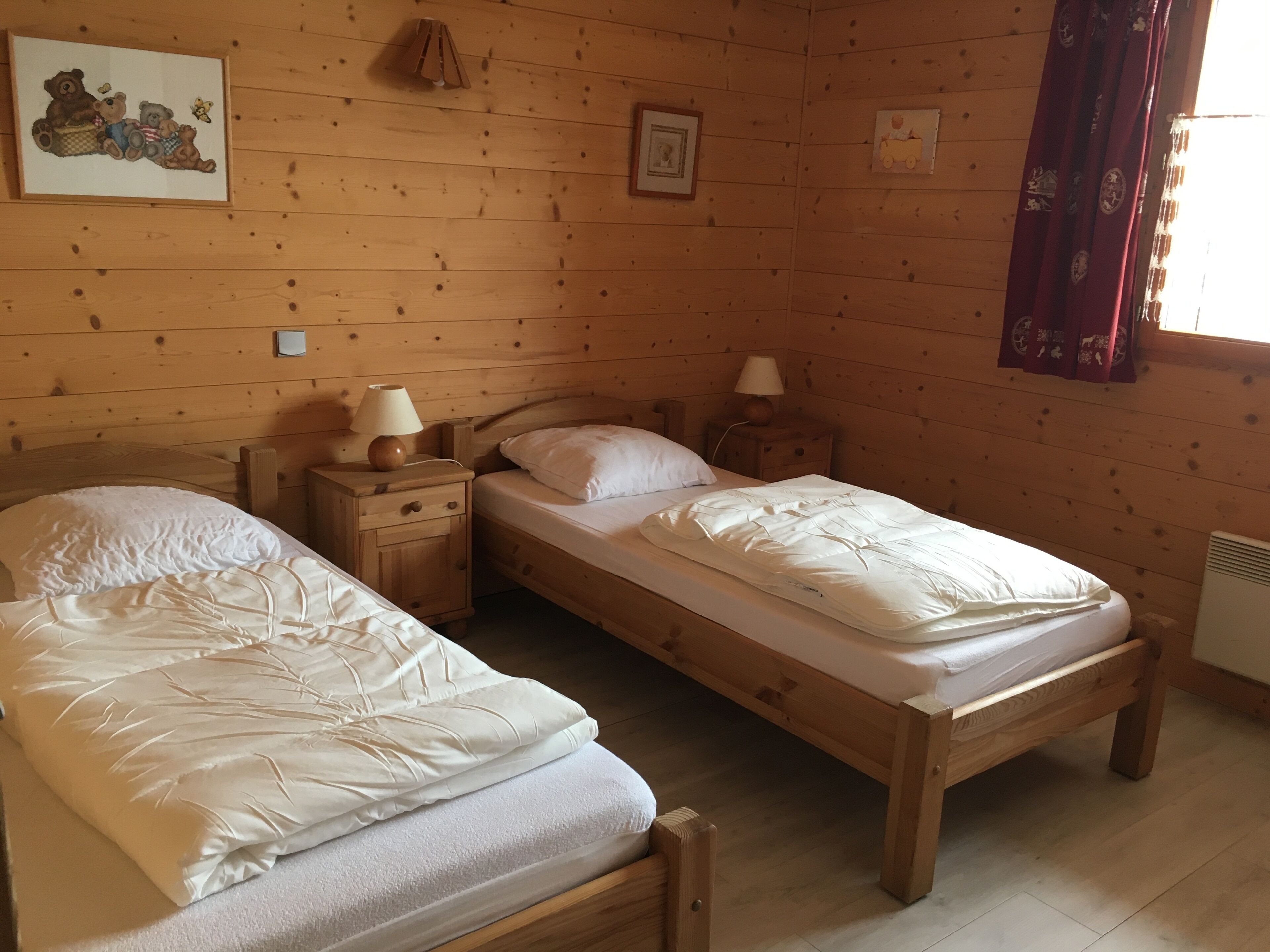Een slaapkamer in een houten hutje met twee eenpersoonsbedden, een nachtkastje met lampen en een lijst aan de muur.